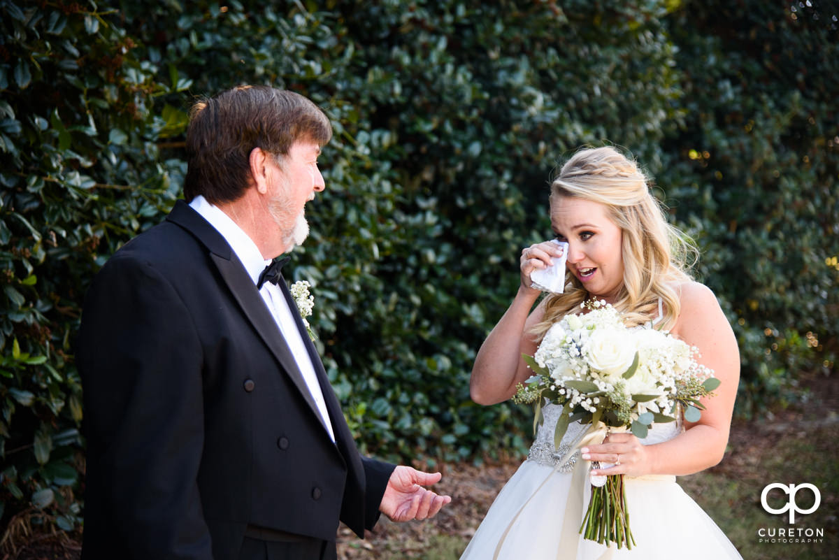 Bride wiping tears from her eye as she sees her father.