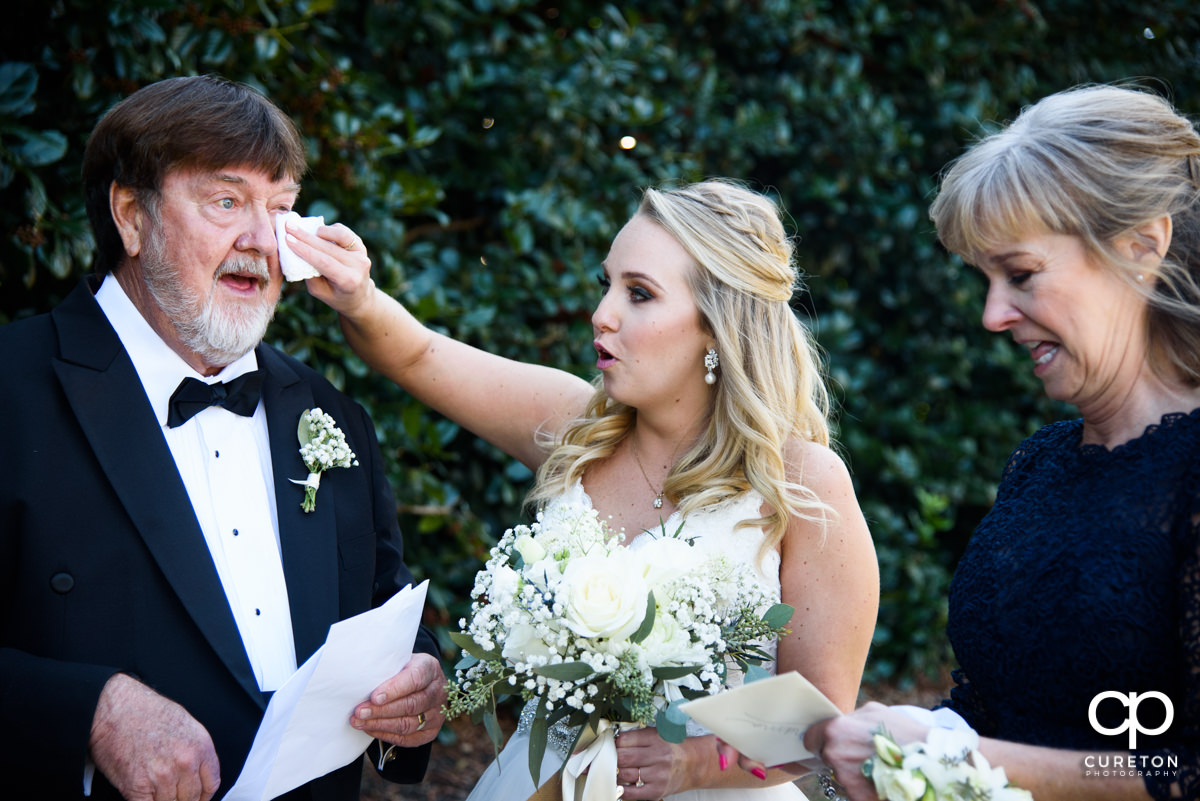 Bride wiping tears from her father's eyes as he sees her for the first time in her dress on her wedding day.