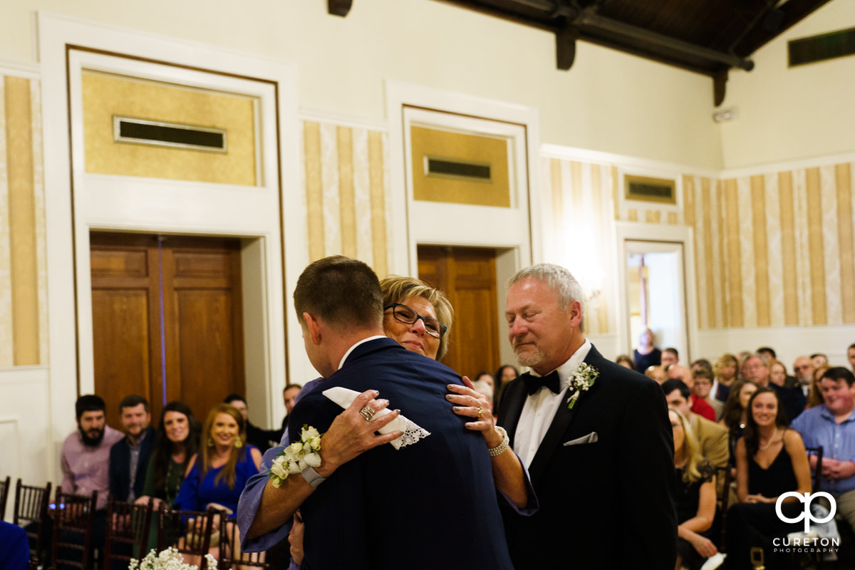 Mother of the groom of hugs her son as he walks her down the aisle.