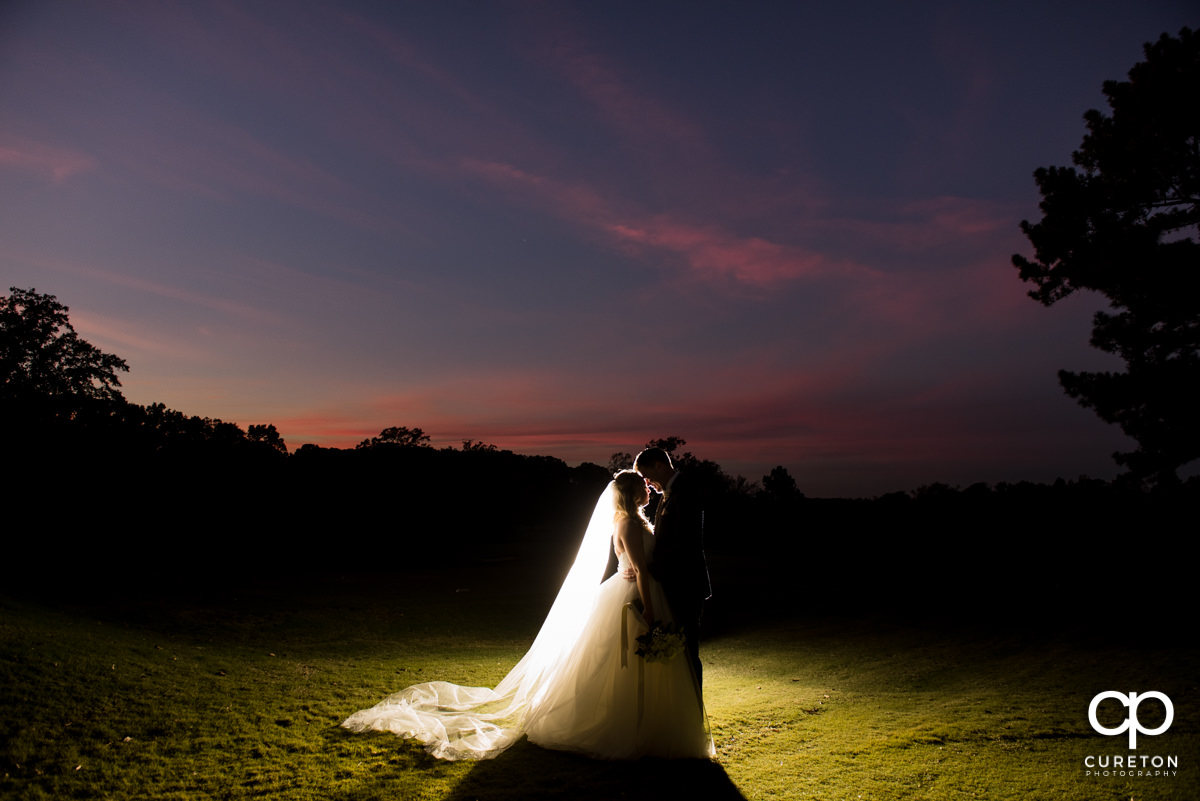 Epic back lit photo of a bride and groom on the golf course at sunset.