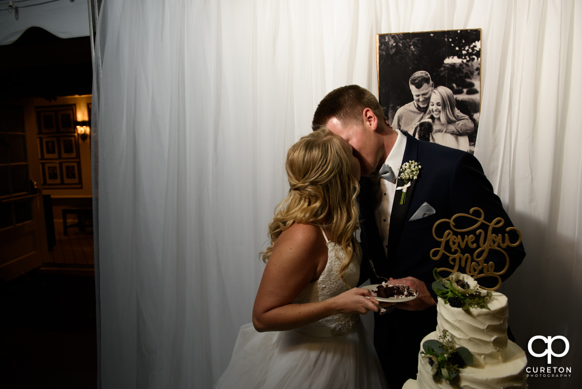 Bride and groom kissing while cutting the cake.
