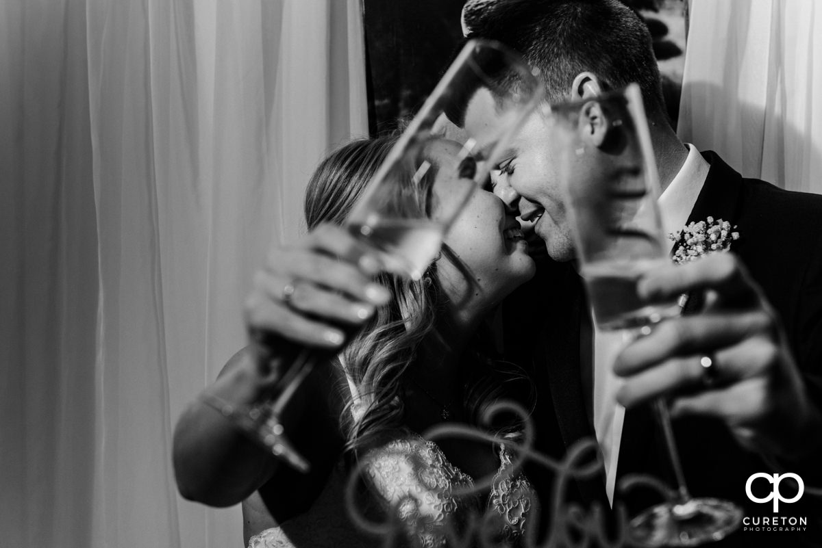 Bride and groom nuzzling with each other behind champagne flutes.