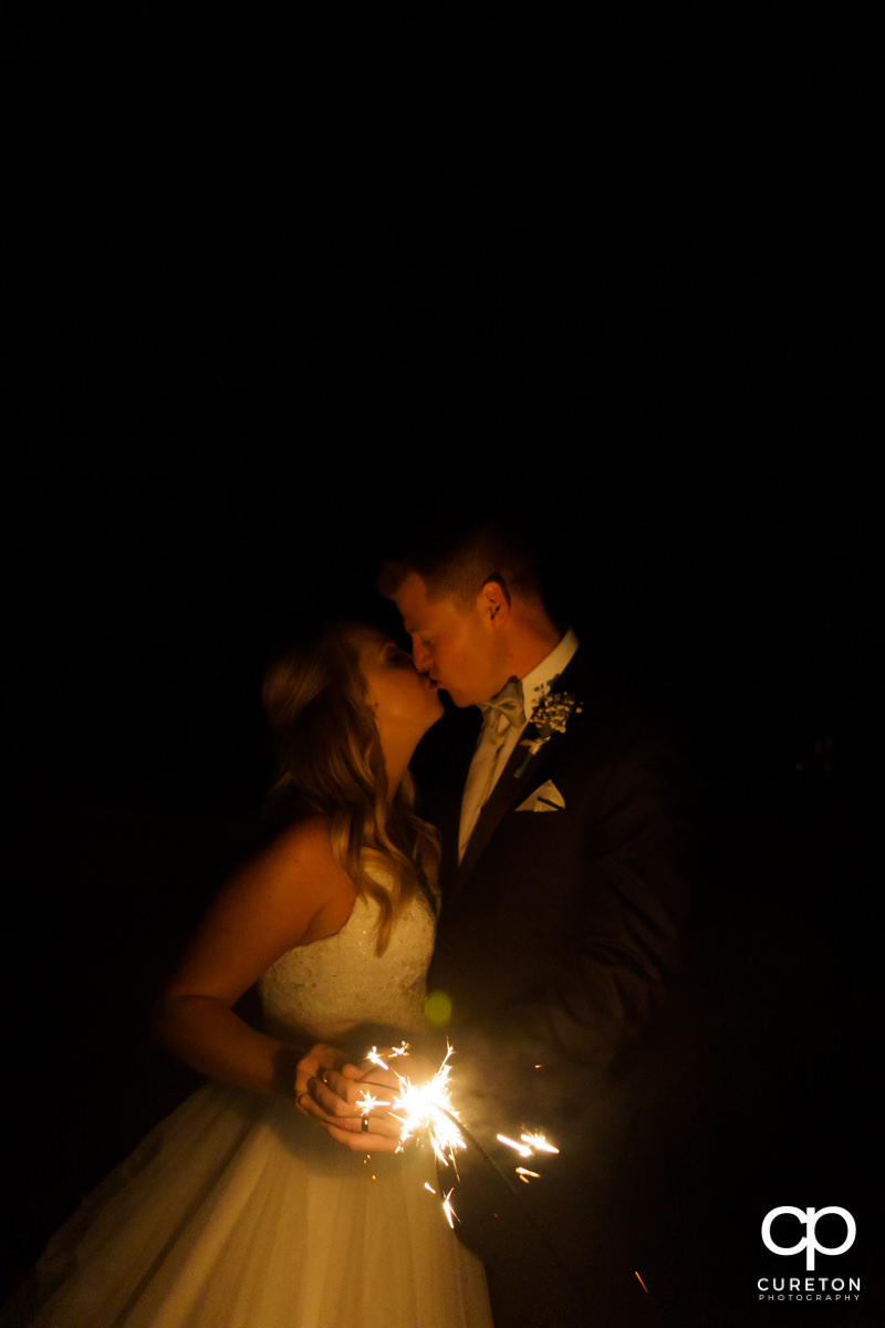 Bride and groom holding a sparkler and kissing.