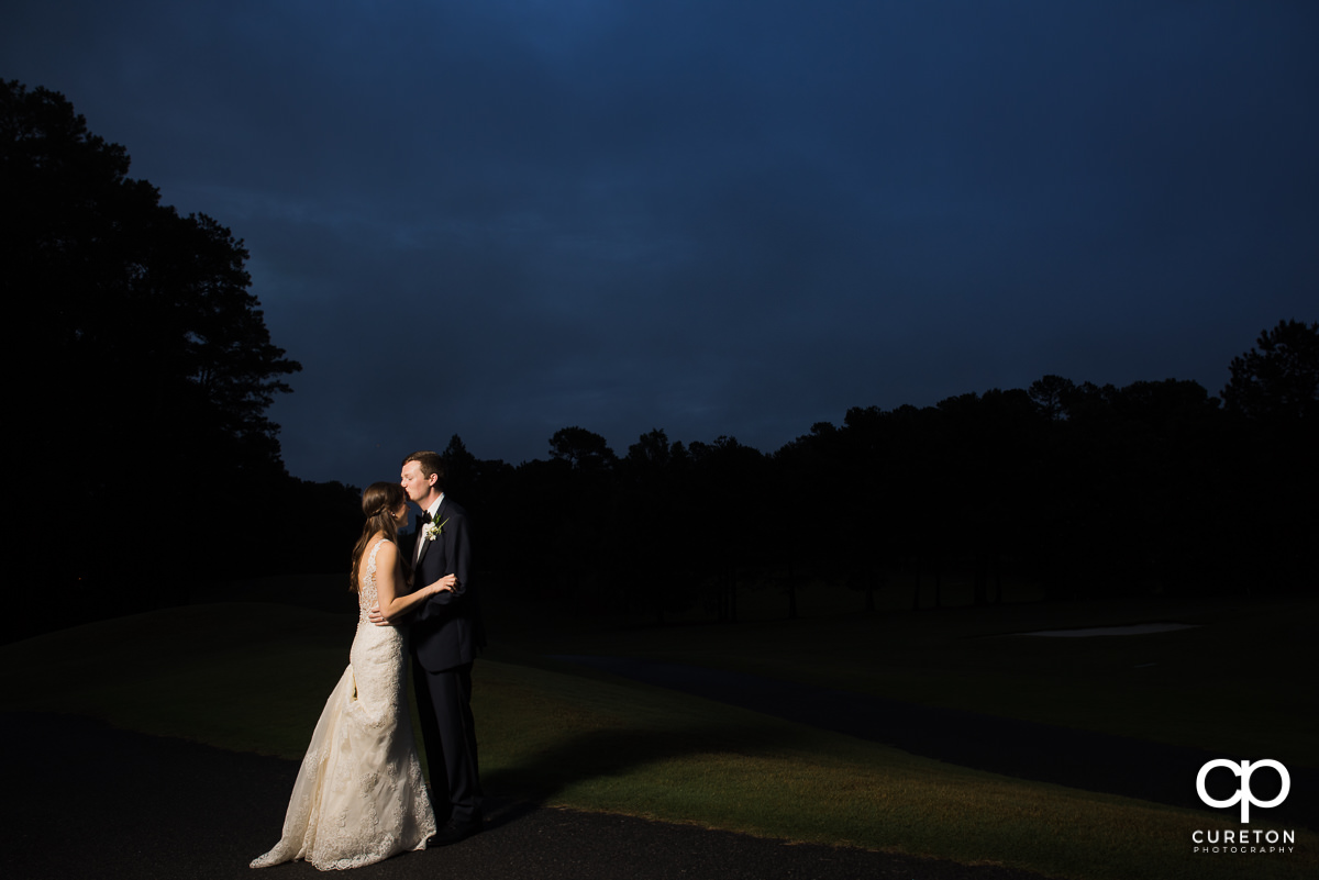 Groom kissing his bride on the forehead at twilight on the golf course at the wedding reception at Spartanburg Country Club.