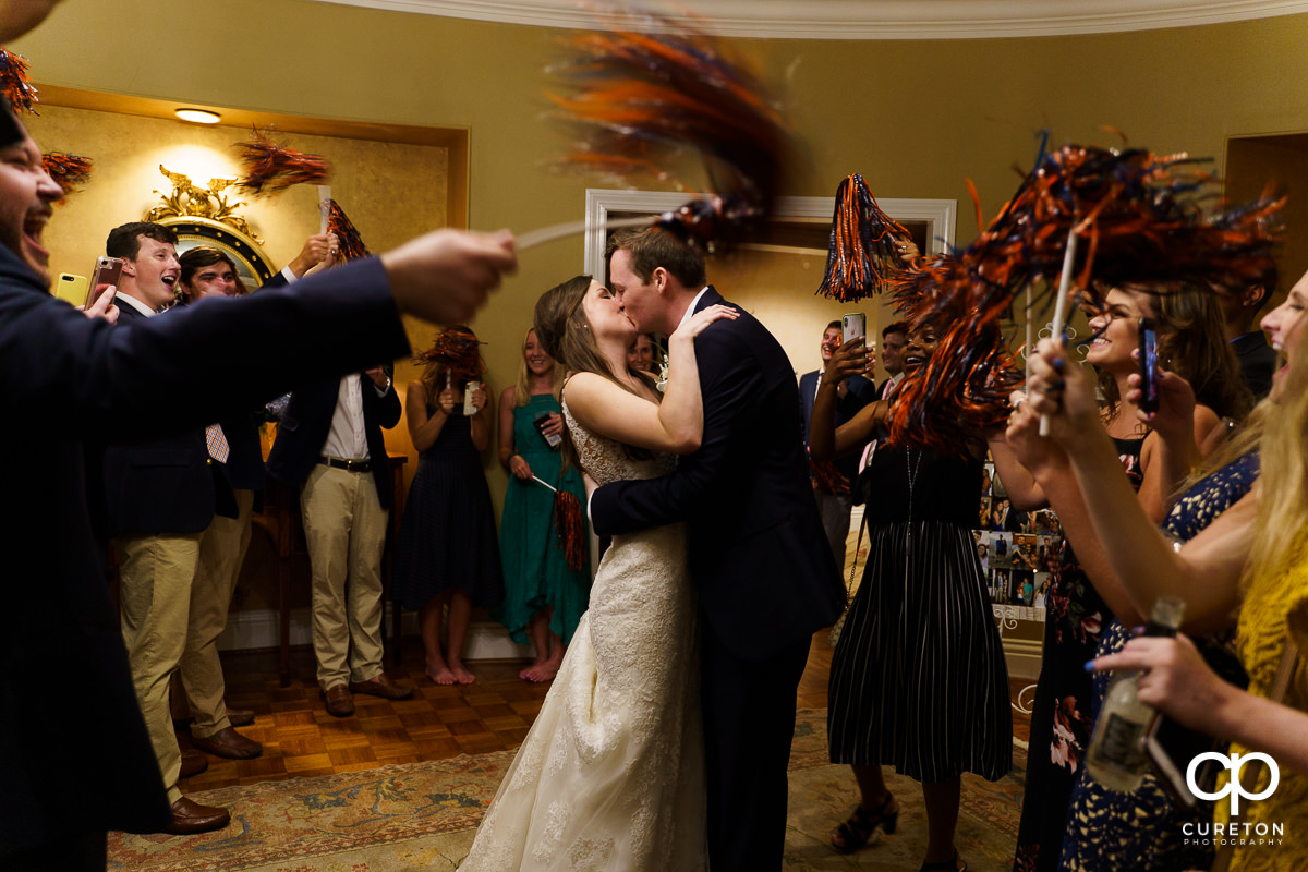 Bride and groom making a grand exit from the wedding reception as guests cheer with Auburn pom poms.