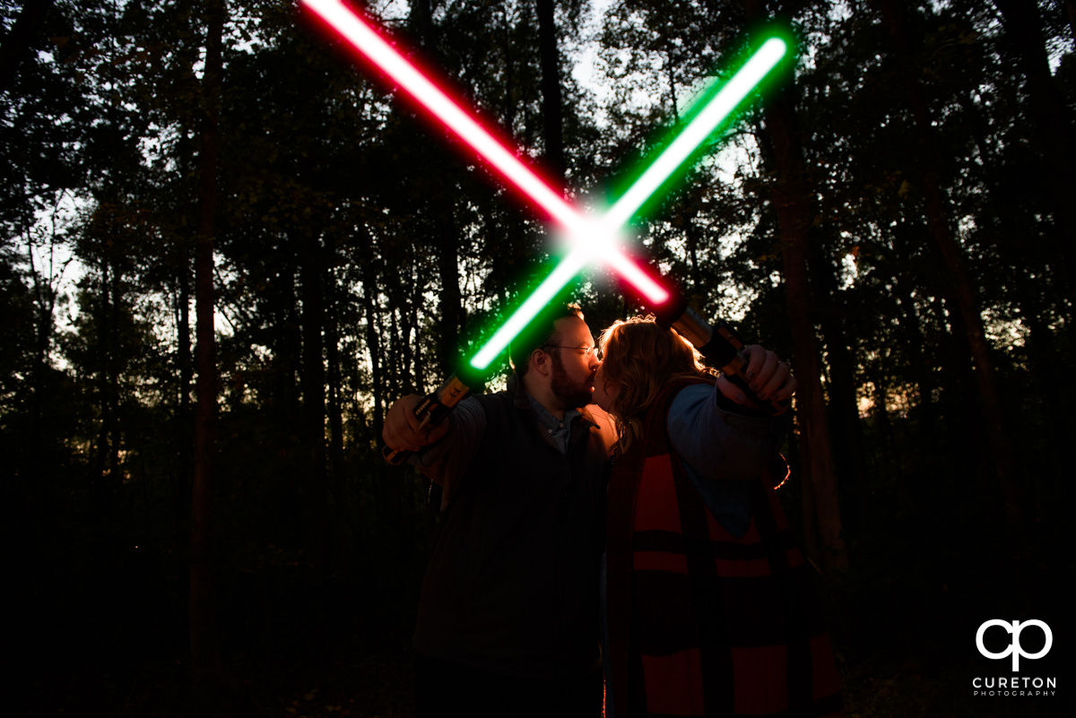 Future bride and groom kissing behind lightsabers at their Star Wars engagement session.