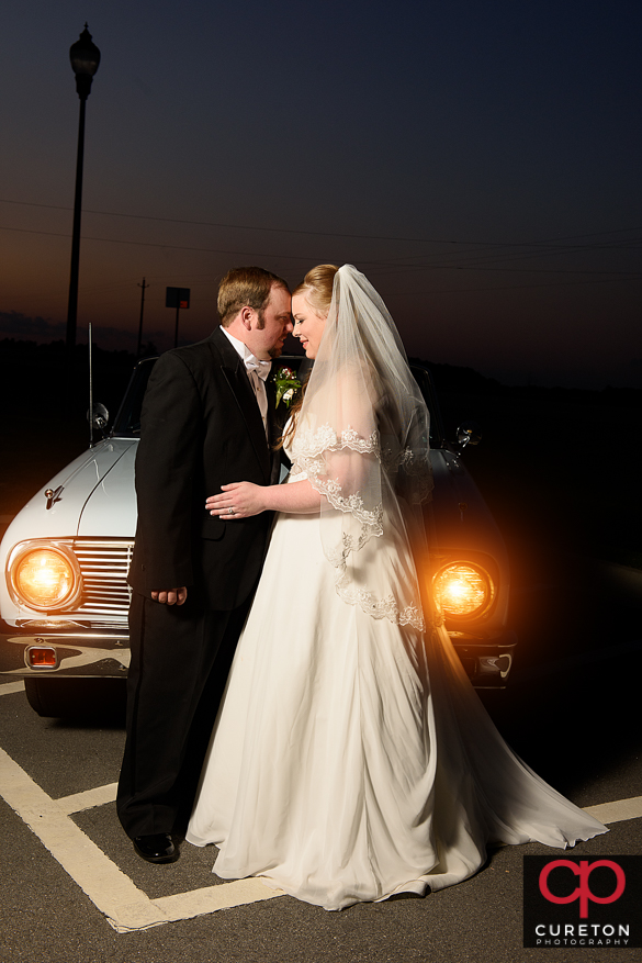 Bride and groom in front of the headlights of a vintage car.