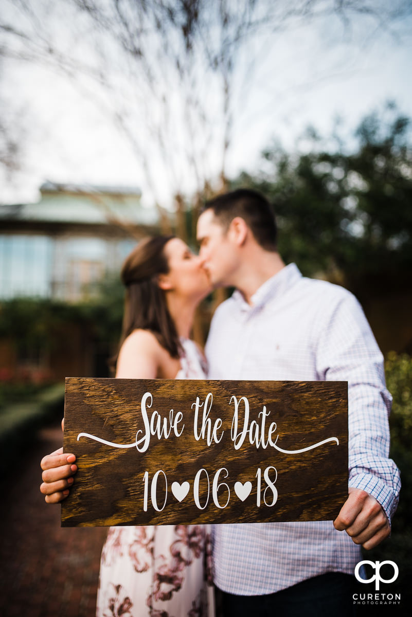 Engaged couple holding up a save the date sign.