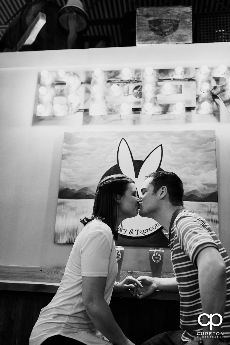 Engaged couple kissing in the Swamp Rabbit Brewery.