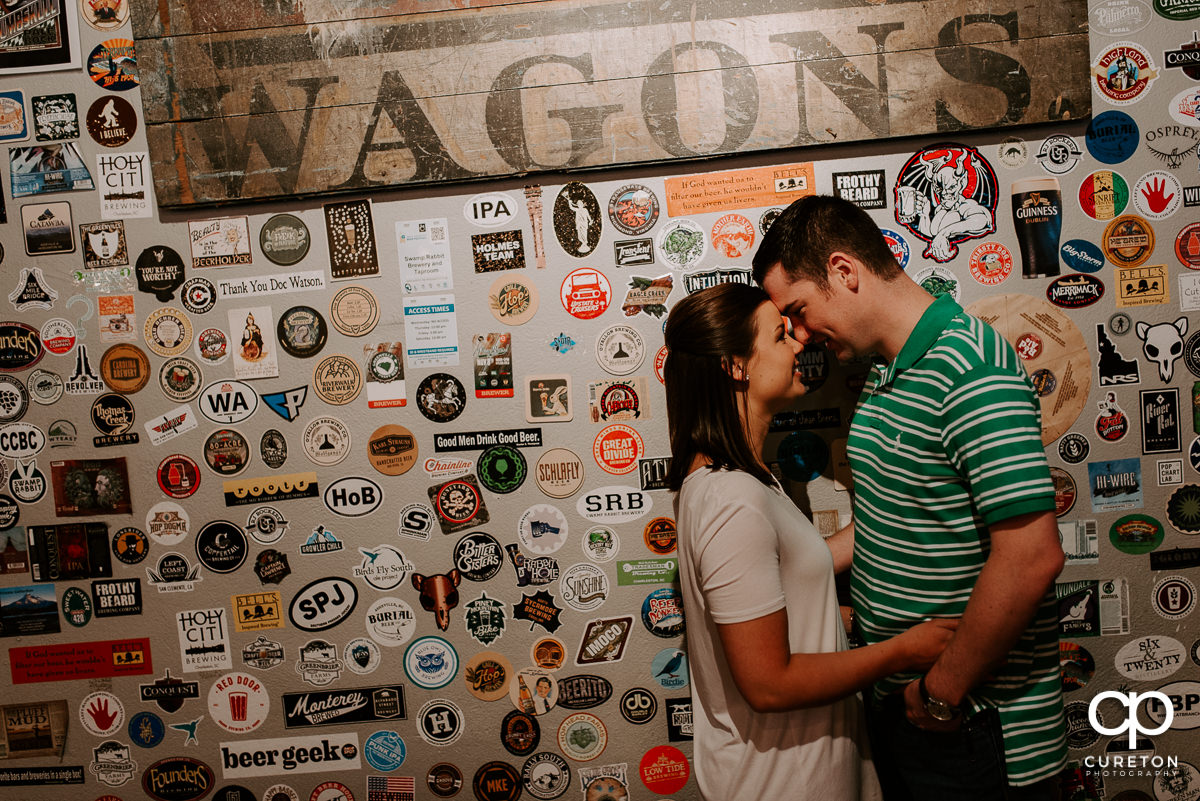 Man and his future bride stanfing in front of a wall of stickers during their Swamp Rabbit Brewery engagement session.