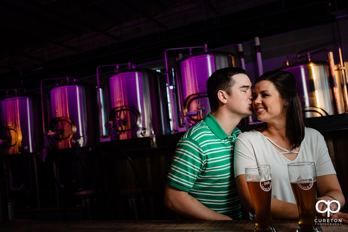 Woman being kissed on the cheek by her future husband during their Swamp Rabbit Brewery engagement session.