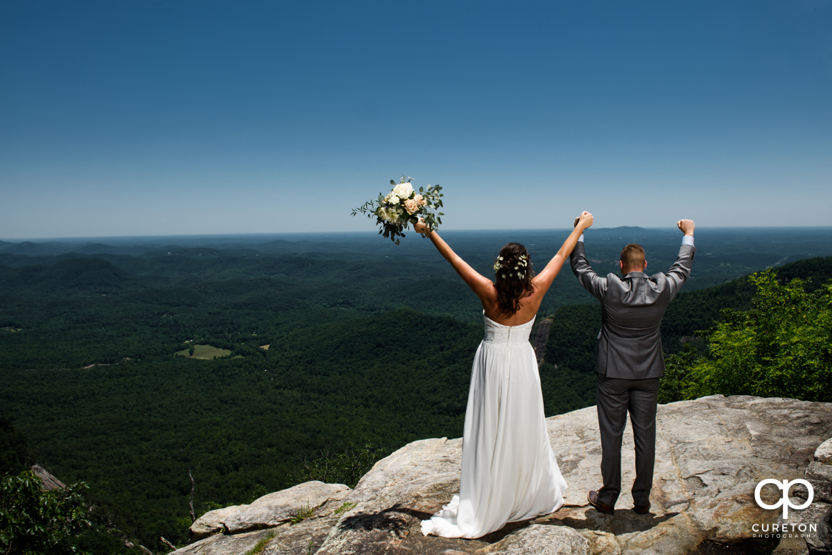 Bride and groom with hands in the air on a cliff at their Pretty Place wedding.