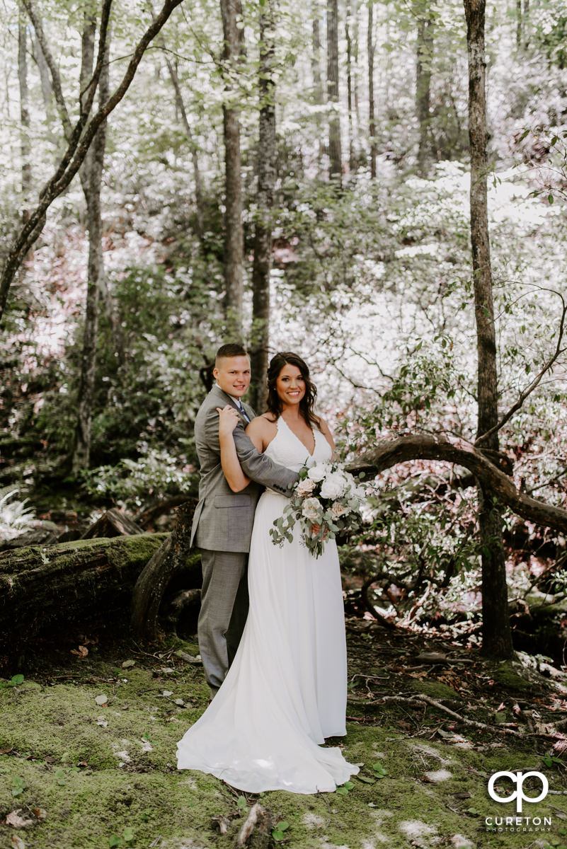 Bride and groom cuddling in the forest.