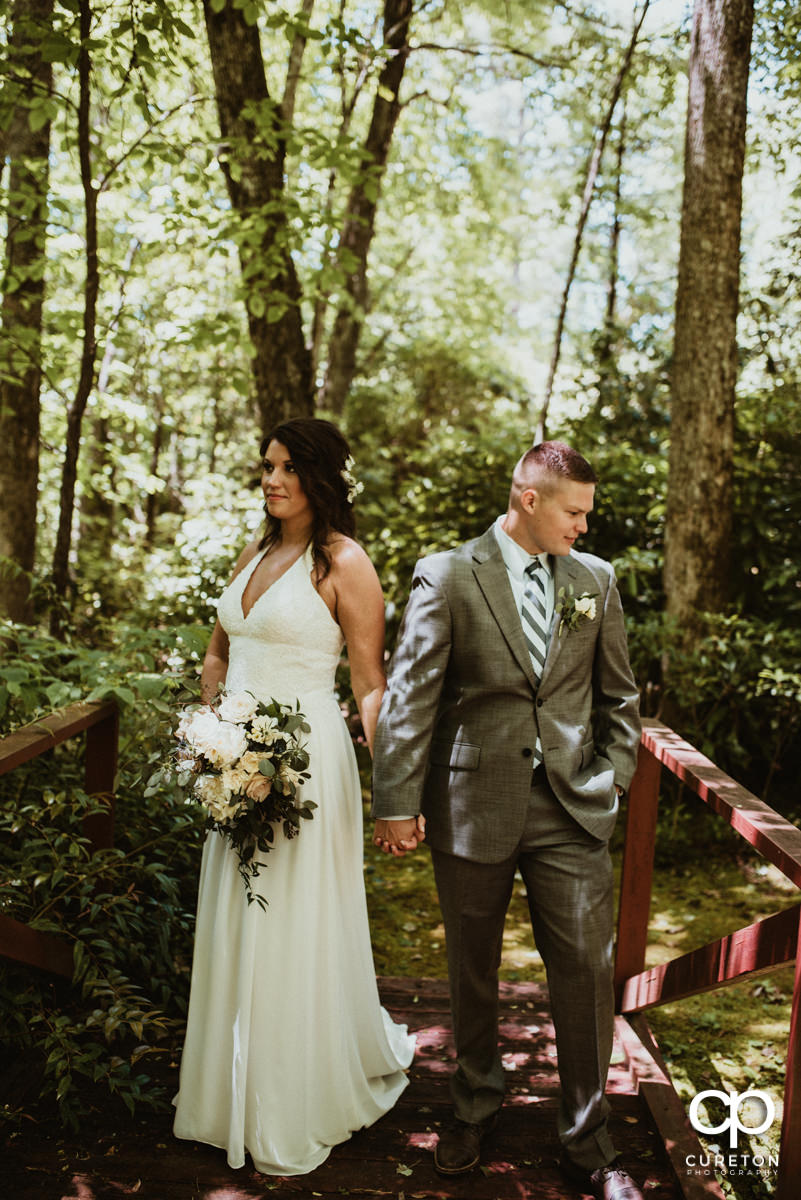 Bride and groom holding hands on a bridge in the woods after their wedding.