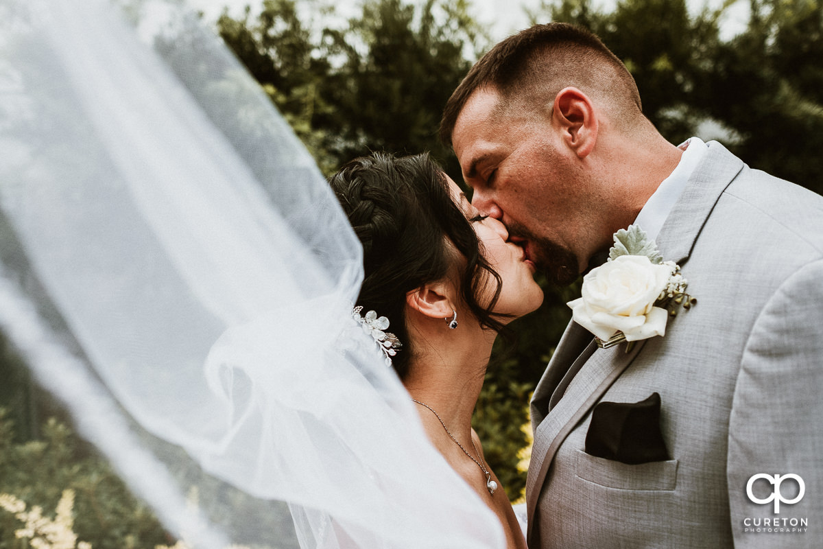 Groom kissing his bride while her veil blows in the wind after their wedding at the Tybee Island wedding chapel .