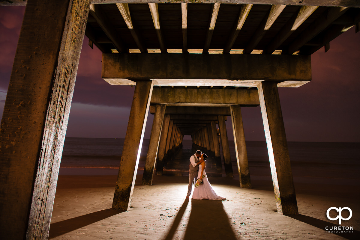 Groom kissing his bride on the beach at sunset underneath the Tybee Island pier after their wedding miles from Savannah,GA .