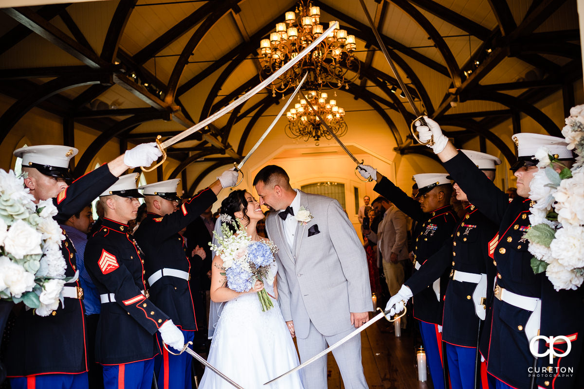 Bride and groom smiling at each other underneath a Marine saber arch at their coastal wedding ceremony.