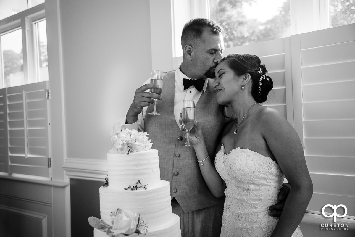 Groom kissing his bride on the forehead after cutting the wedding cake.