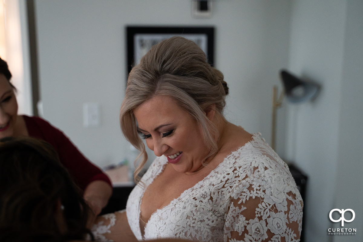 Bride smiling as she puts on her dress.