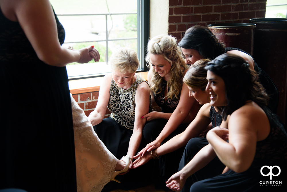Bride's mom and bridesmaids helping the bride with her shoes.