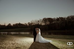 Bride and groom kissing in front of a pond at sunset.