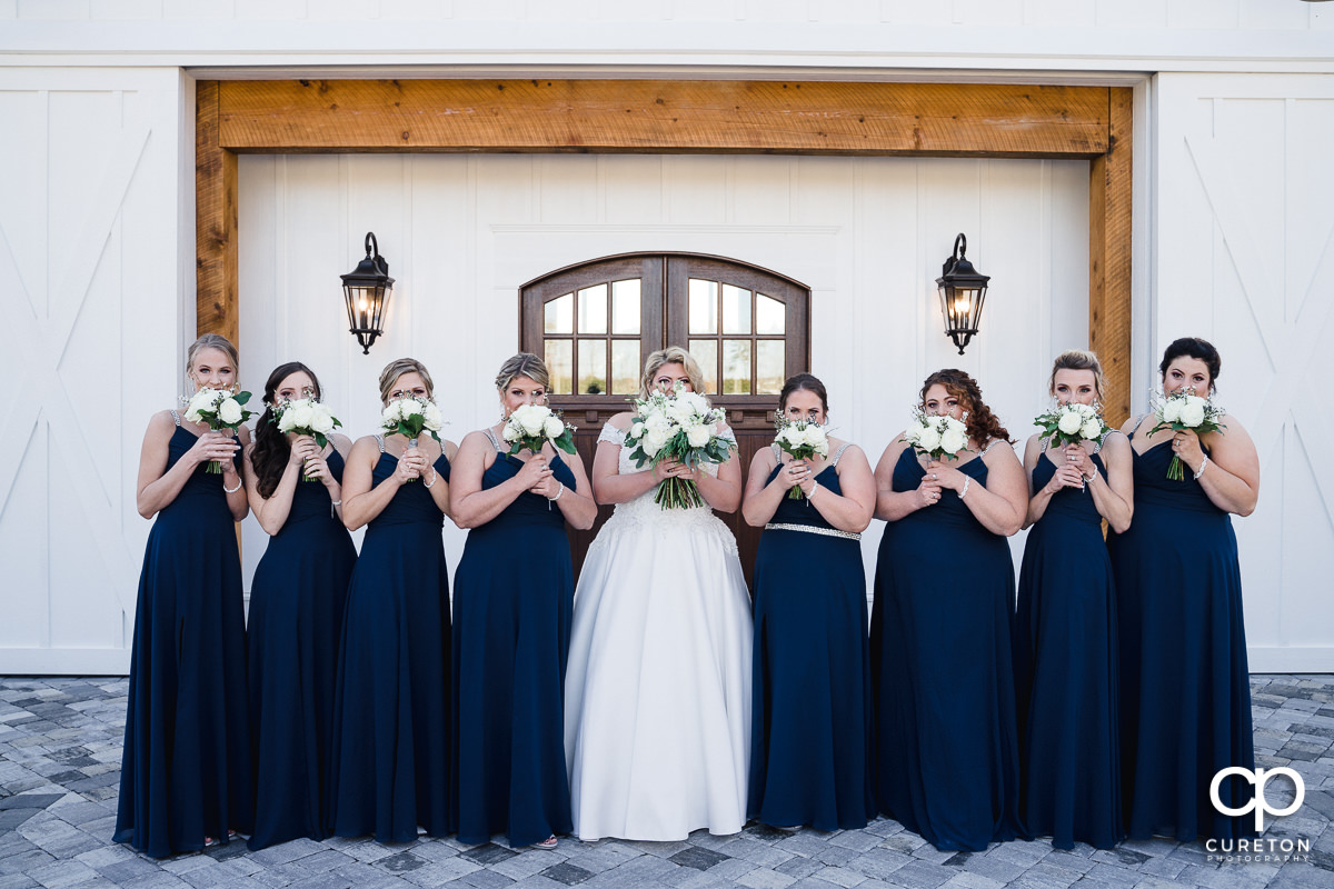 Bride and bridesmaids holding flowers over their faces.