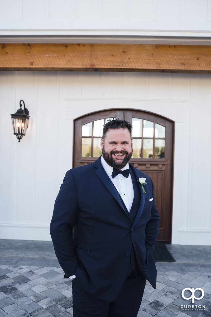 Groom in front of a white barn.