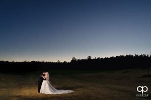 Bride and groom dancing in a field at sunset.