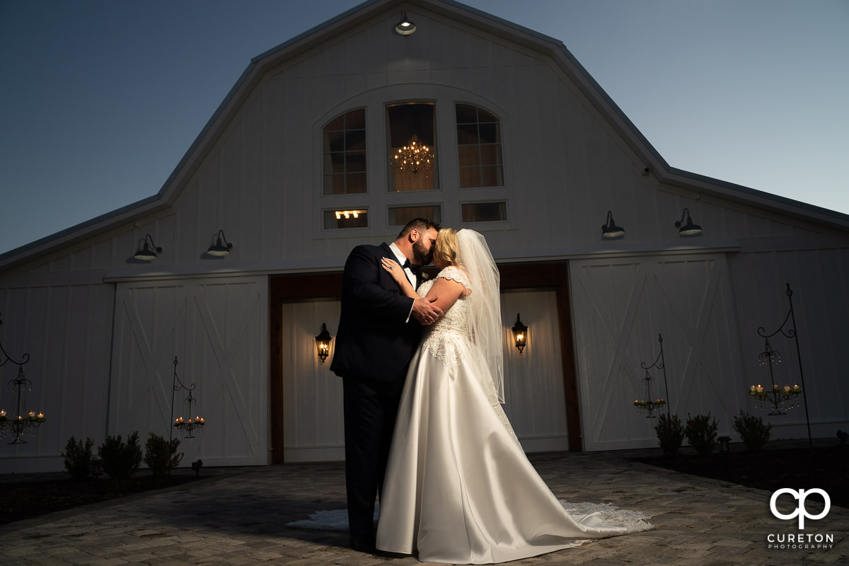 Bride and groom kissing in front of Heyward Manor at sunset.