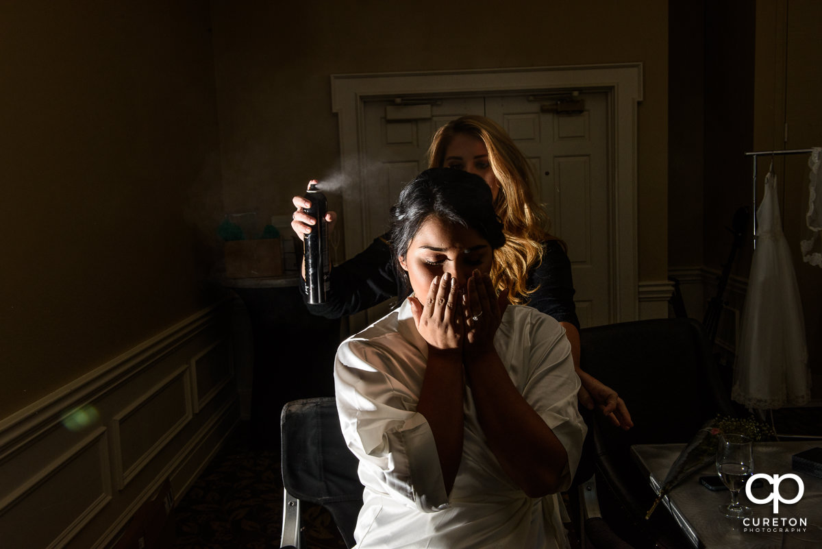 Bride having hair spray applied.