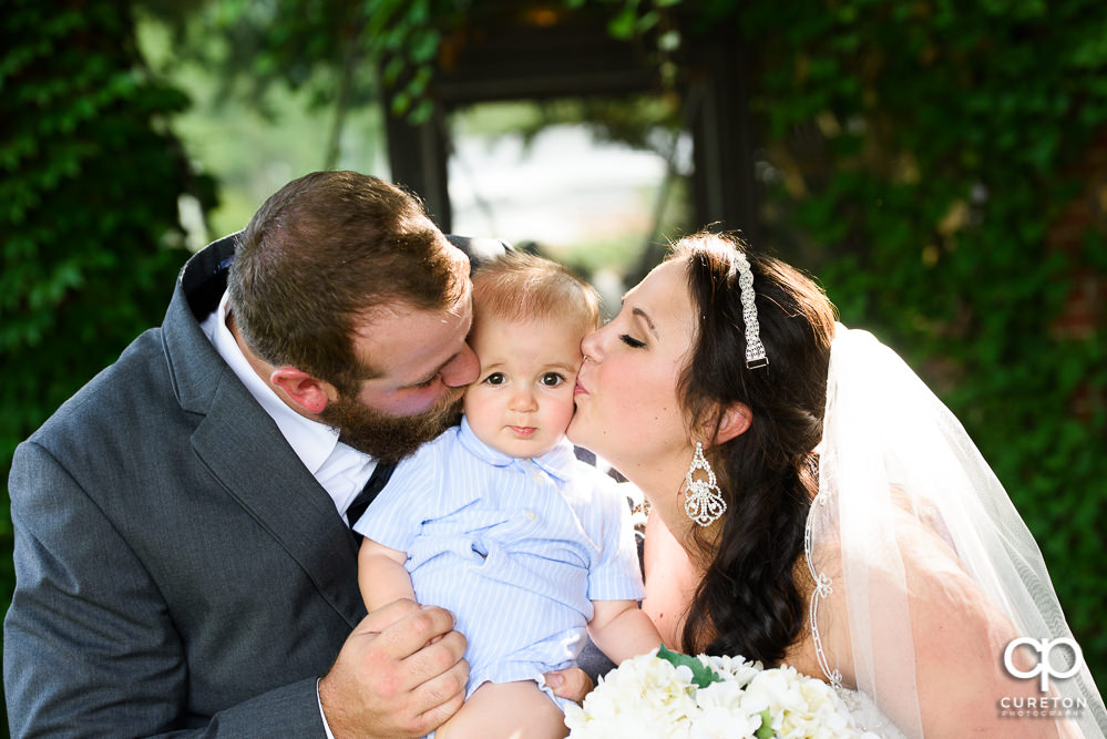 Bride and groom kissing their infant son.