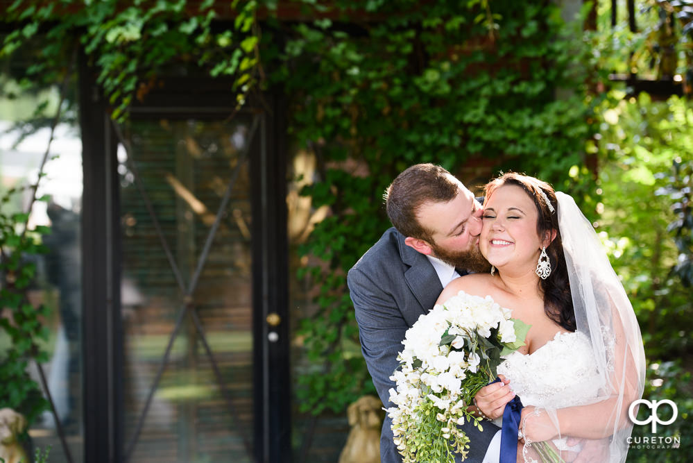 Groom hugging his bride tight and kissing her on the cheek after their wedding at the Simpsonville venue The Loom.