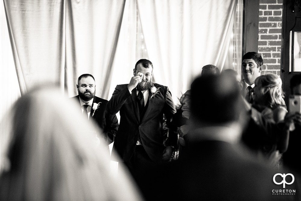 Groom tearing up as he sees his bride for the first time walking down the aisle during their wedding ceremony at The Loom at Cotton Mill Place.
