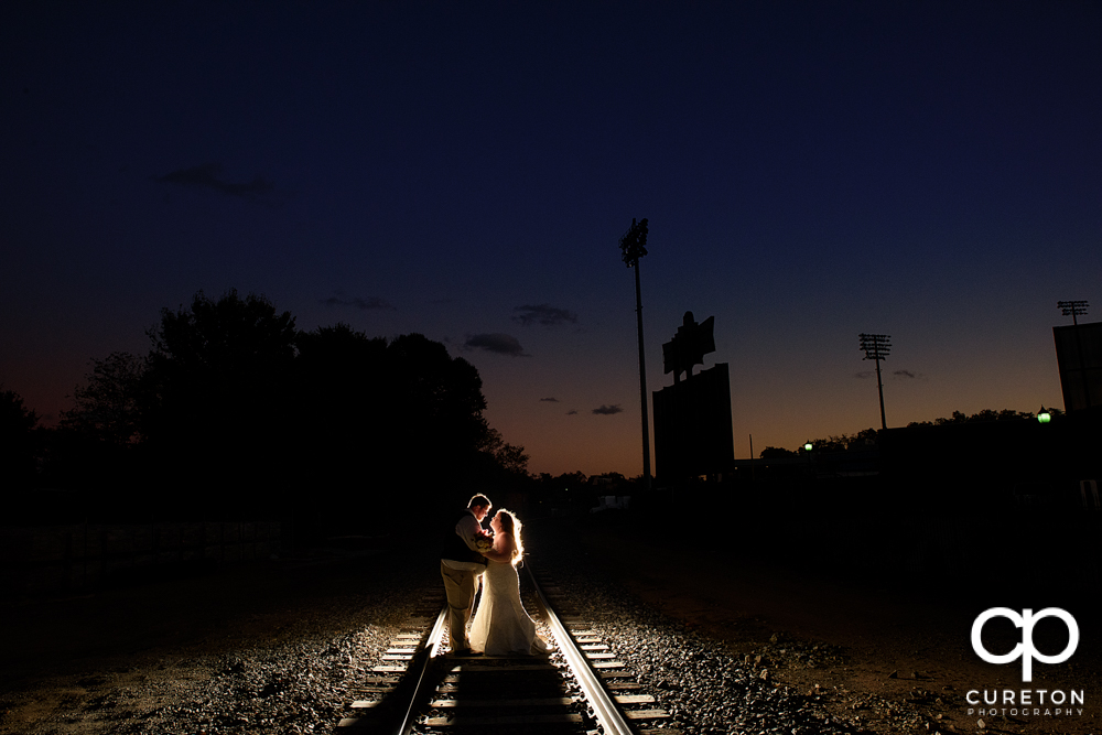 Bride and groom on railroad tracks near Fluor Field at sunset.
