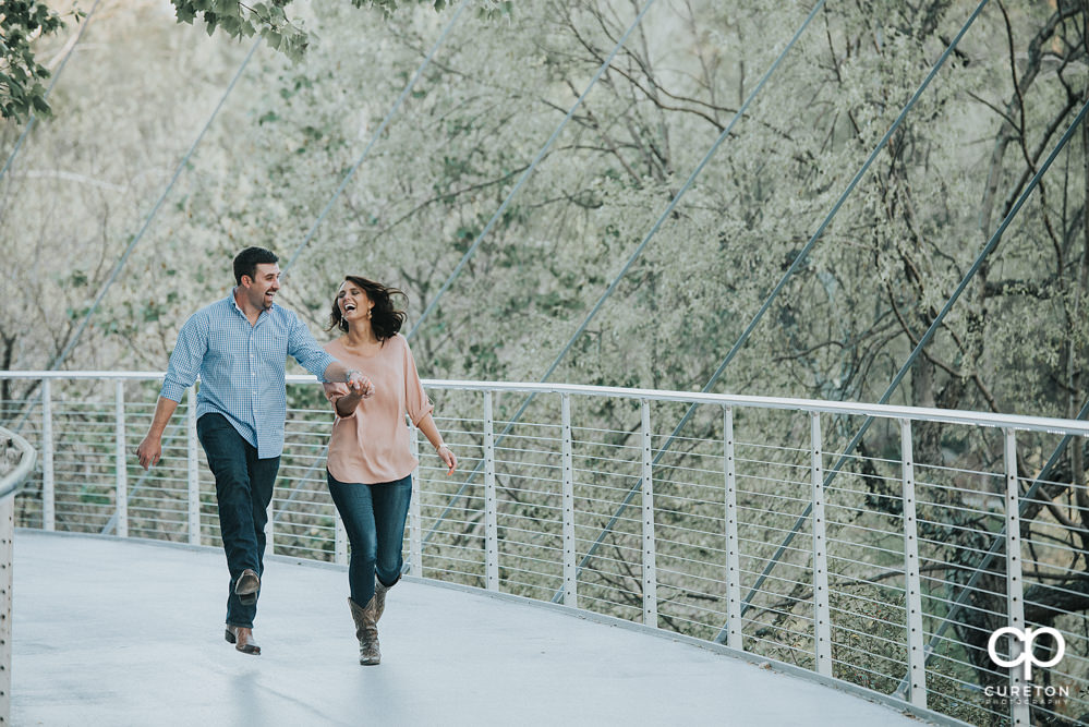 Engaged couple skipping on Liberty Bridge in Falls Park during their engagement photo session.