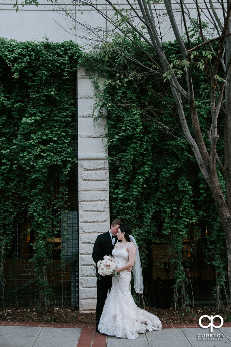 Bride and groom standing in front of greenery on a street in downtown Greenville,SC.