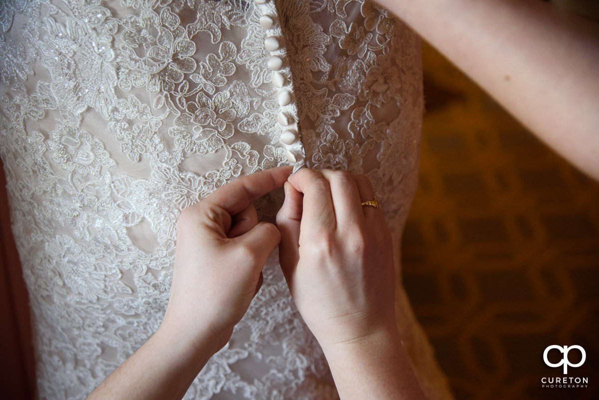 Bridesmaids helping the bride button her dress.