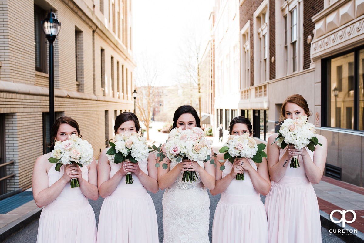 Bridesmaids holding flowers over their faces.