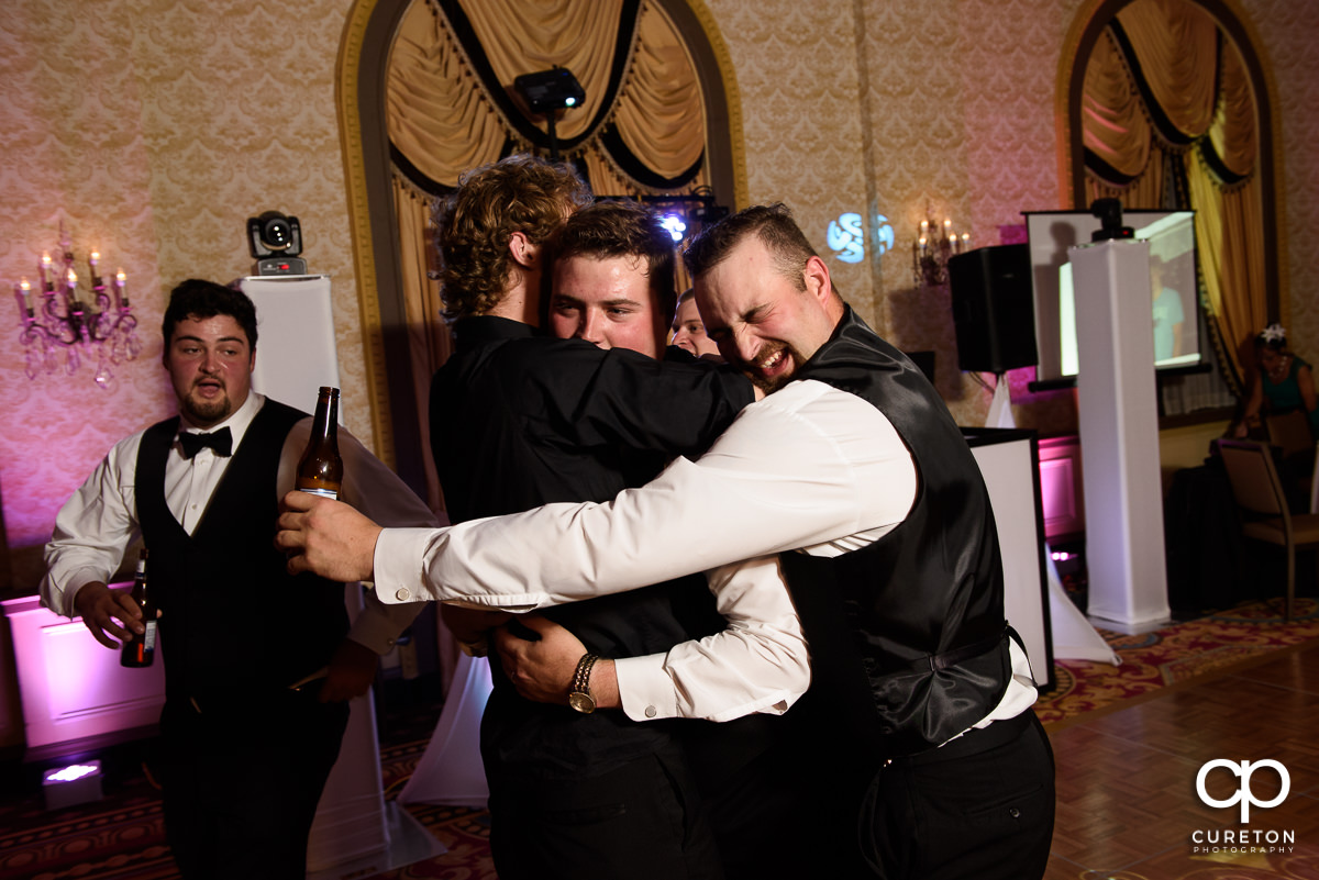 Groomsmen hugging the groom on the dance floor.