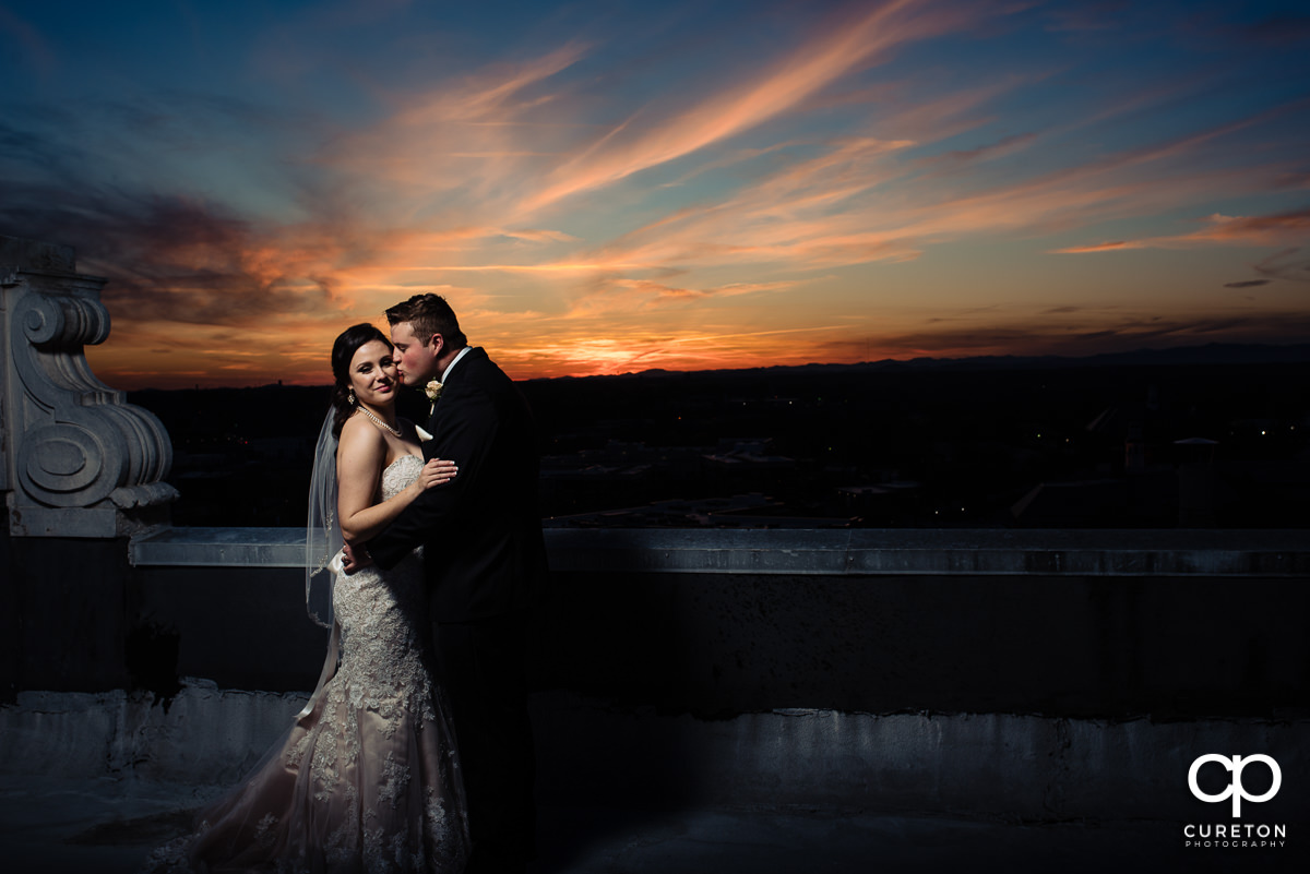 Groom kissing his bride on the rooftop.