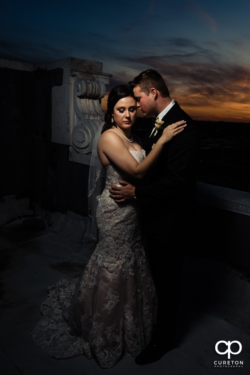 Bride and groom snuggling at dusk on the rooftop of the Westin Poinsett Hotel after their wedding ceremony.