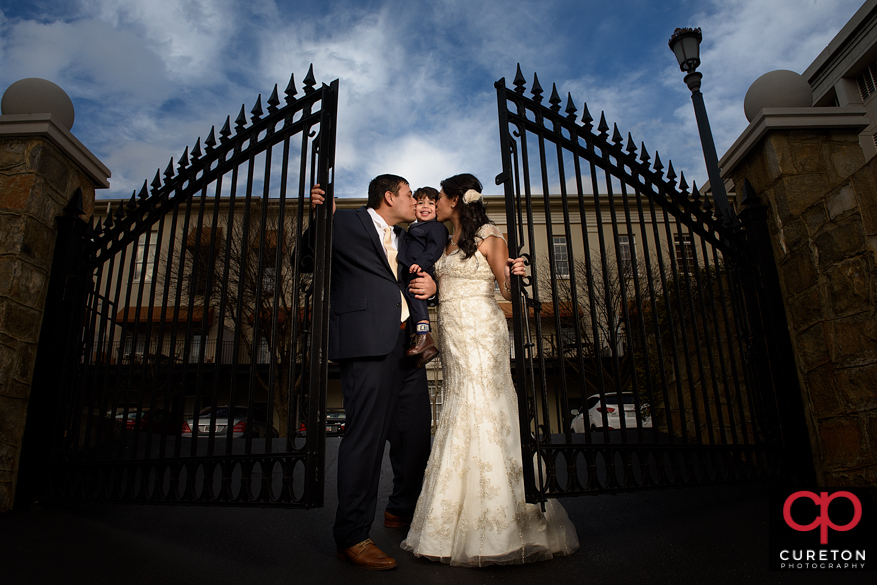 Bride, groom, and son, near a gate in Greenville.