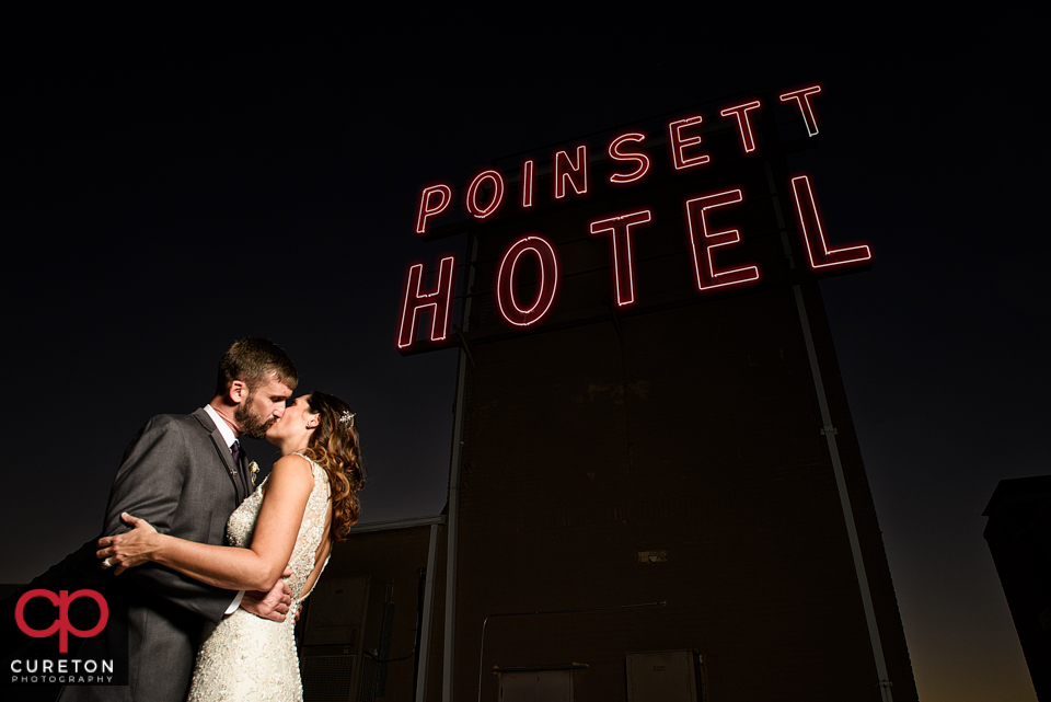 Epic shot of a bride and groom kissing near the sign on the Westin Poinsett rooftop during their wedding reception.