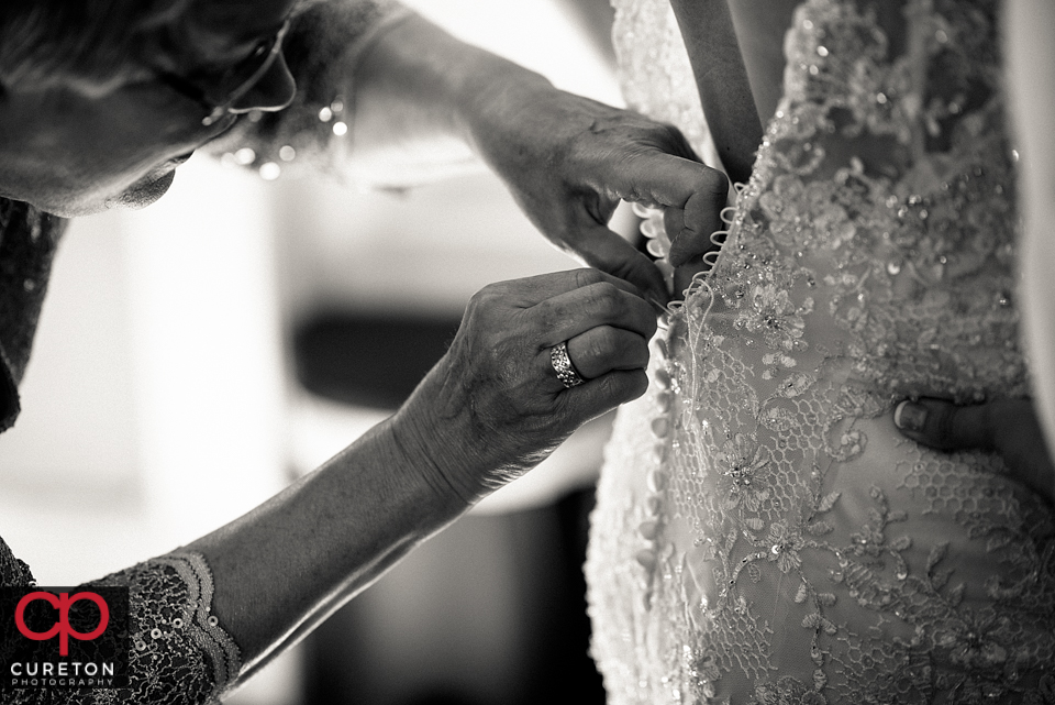 Brides mom buttoning the back of the brides dress.