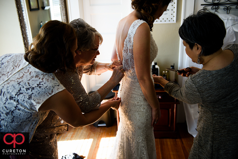 Bridesmaids helping the bride into her dress.