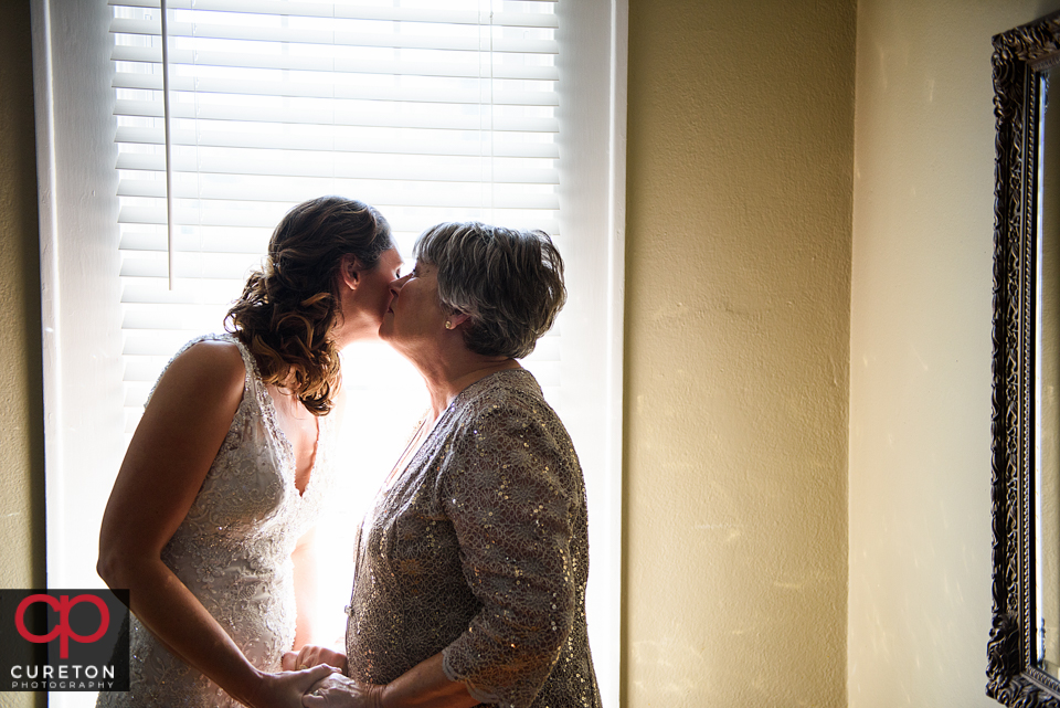 Bride's mom kissing the bride on the cheek.