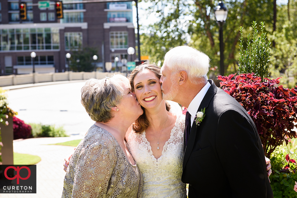 Brides parents both kissing her on the cheek after her wedding.
