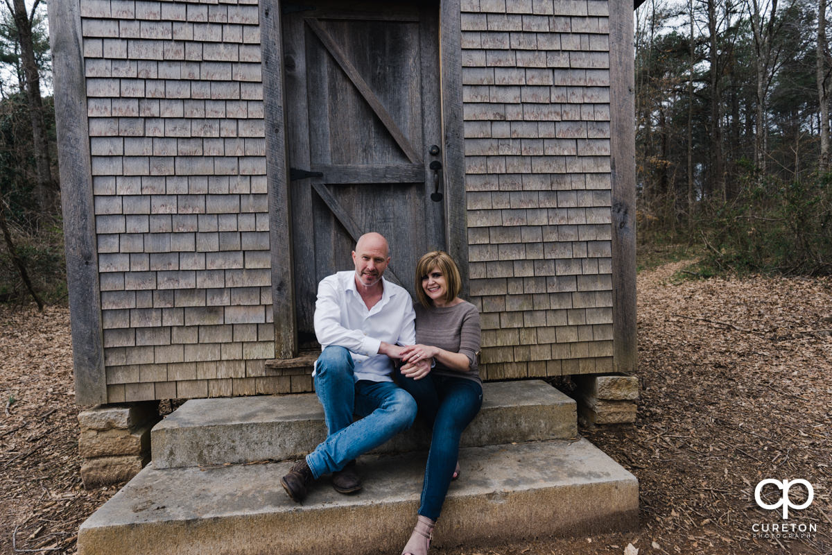 Man and woman sitting on the steps of a rustic cabin during a Furman University winter Engagement session in Greenville,SC.
